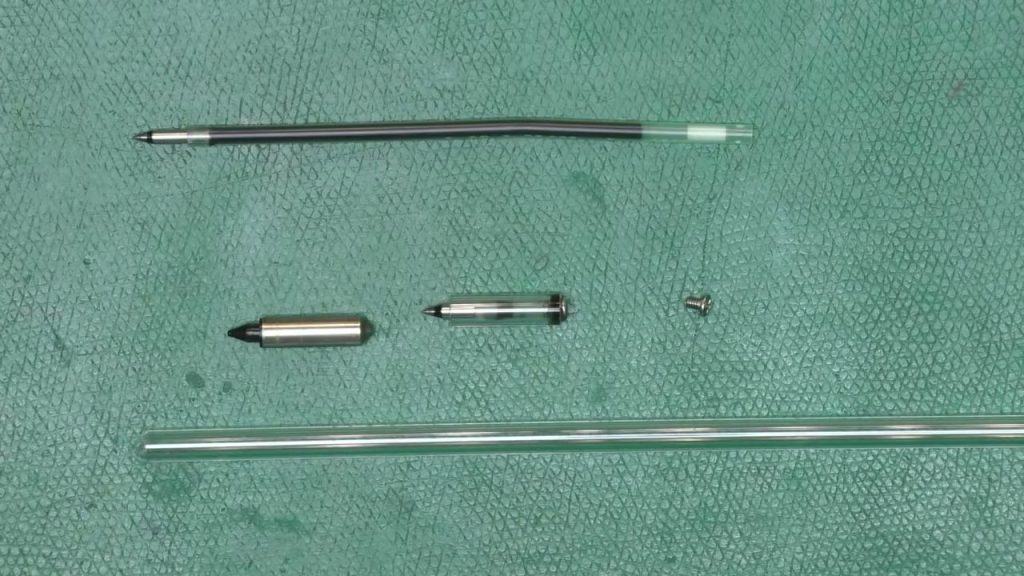 Parts for a DIY Alps plotter pen on a green cutting mat: a pen refill, two small pen bodies, an M2 screw and a length of clear acrylic tubing
