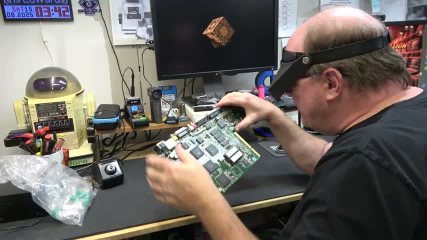 Chris Edwards holds an exposed Amiga 1200 circuit board at his repair bench